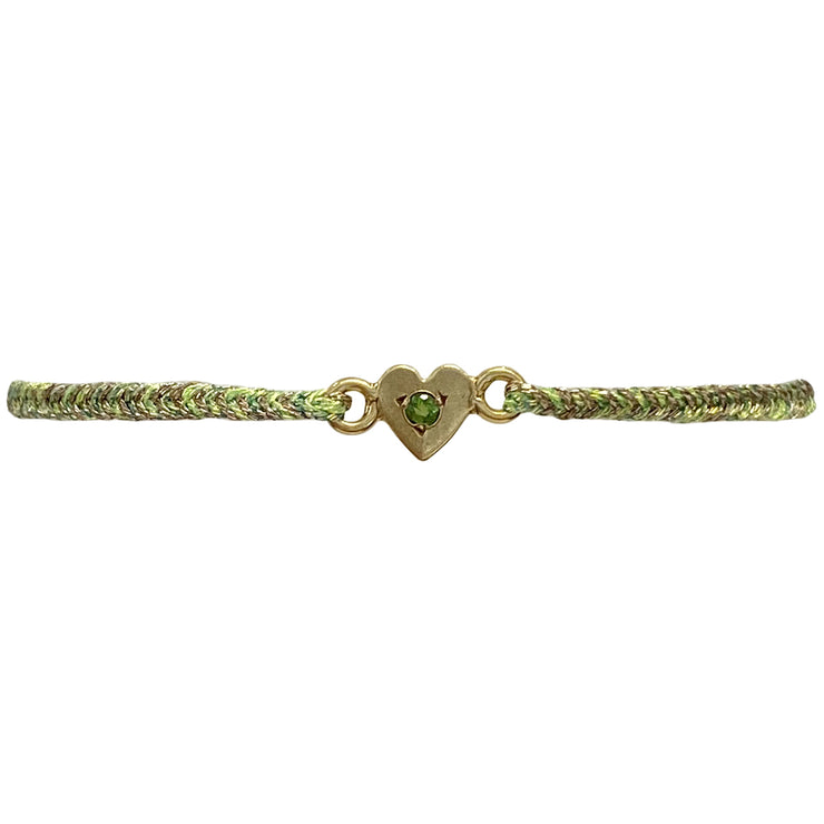 This delicate bracelet is handmade by our team of master artisans using metallic threads and a gold heart charm encrusted with a sparkling green tourmaline stone. It&