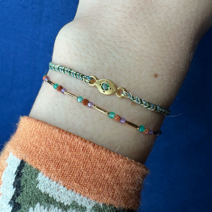 This delicate bracelet is handmade by our team of master artisans using metallic threads and a gold eye charm encrusted with a beautiful green tourmaline stone. It&