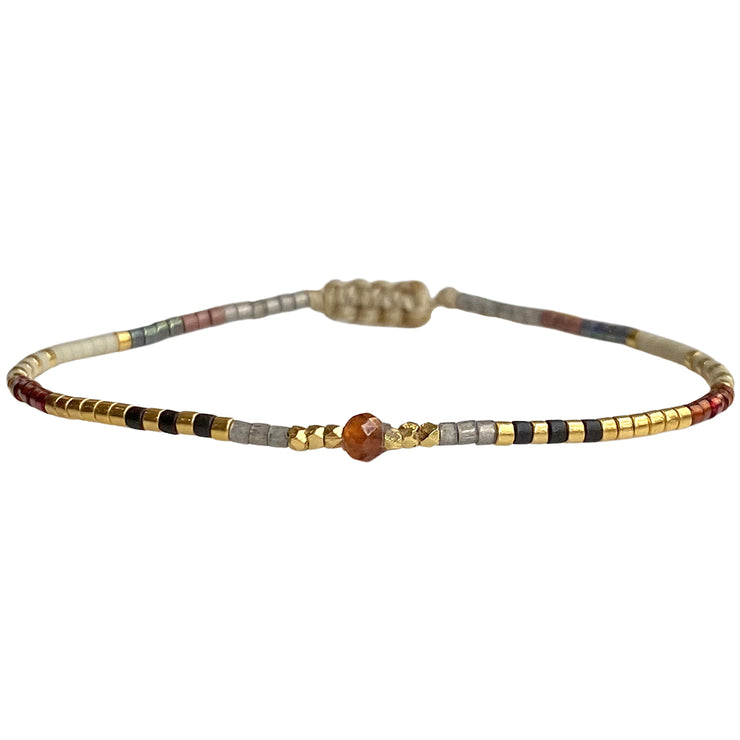 Handwoven in Colombia, this delicate bracelet features a single row of Japanese glass beads in gold and neutral tones with a Hessonite, stone of happiness, in the centre.  Wear this stylish bracelet alone or as a part of a bracelet layering combination, with your favourite outfits.  Details:  - Japanese glass beads  - Gold vermeil faceted beads  - Hessonite semi-precious stone  - Width: 2mm  -Can be worn in the water