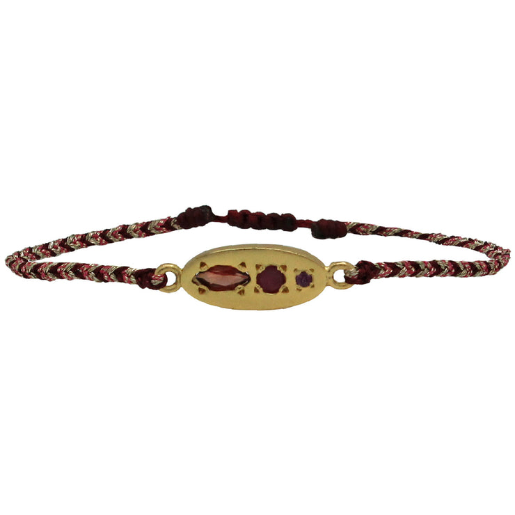 This luxurious handwoven bracelet features a gold centrepiece with Precious Garnet and Ruby stones. This beautiful bracelet in burgundy tones will undoubtedly become an essential piece in your collection.  Can be worn alone as a statement or with other favourite accessories all season long.  Details:      3 Precious stones; Garnet and Ruby     Handwoven adjustable bracelet     Metallic threads     Vermeil on sterling silver center piece 